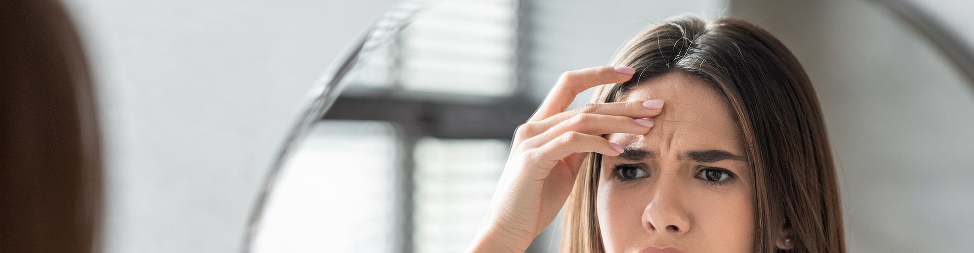 Unhappy Young Woman Looking In Mirror And Touching Wrinkles On Her Face