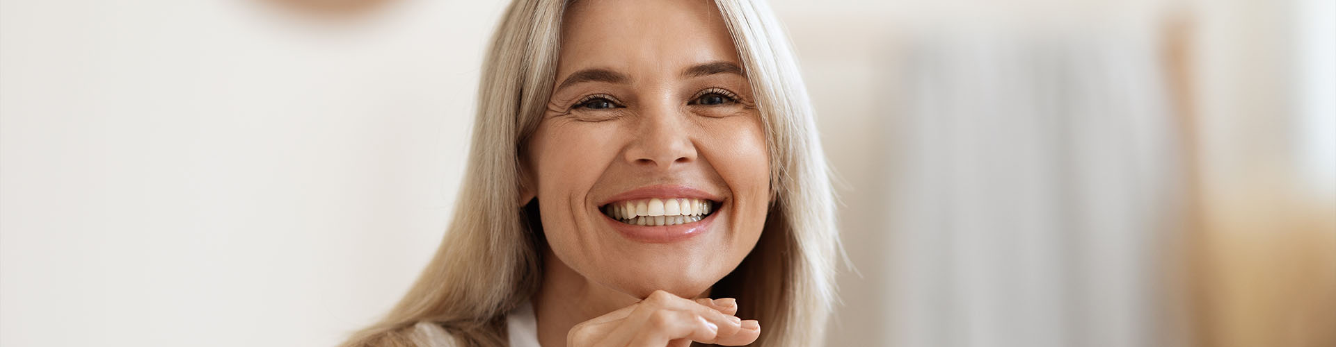 Happy attractive blonde woman in white silky bathrobe posing at white bathroom, smiling at camera
