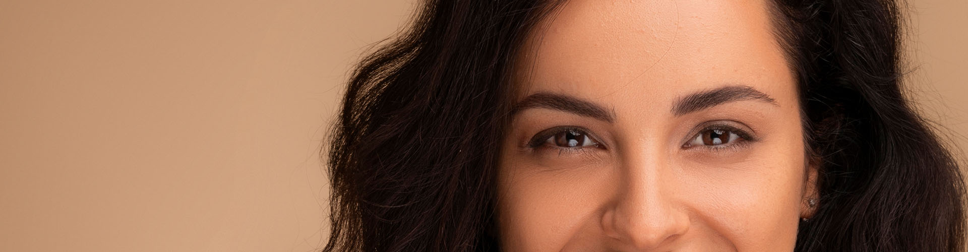 Portrait of beautiful brunette long-haired millennial woman posing on beige studio background