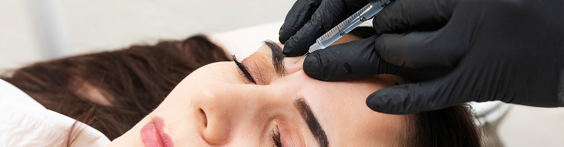Close up of the hands of a cosmetologist injecting Botox into a woman's forehead